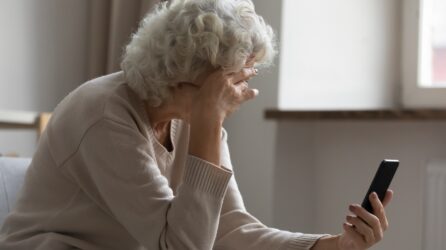 Elderly woman on the phone, holding her head in her hand