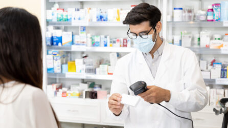 A pharmacist scans the barcode of a prescription while a customer waits
