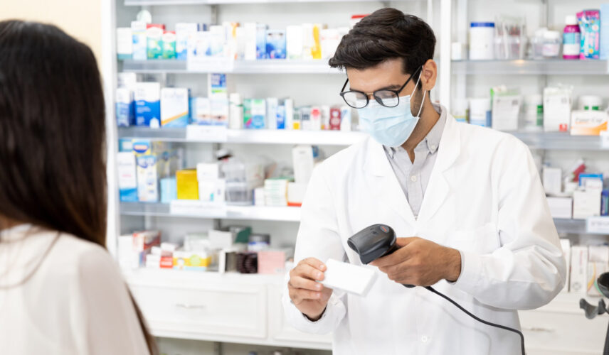 A pharmacist scans the barcode of a prescription while a customer waits