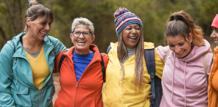 Women of several ages and ethnicities smiling and laughing while embracing outdoors
