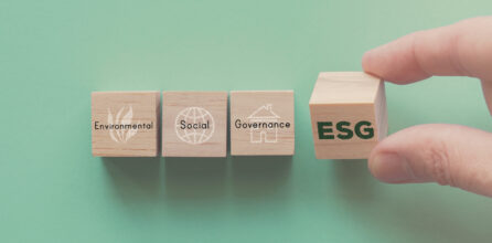 A hand holding a wooden block with the letters ESG on it, next to blocks that read "Environmental," "Social," and "Governance"