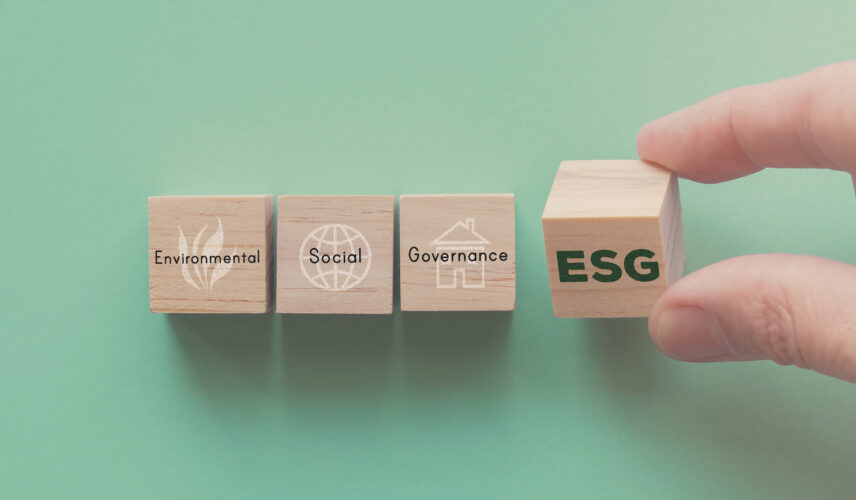 A hand holding a wooden block with the letters ESG on it, next to blocks that read "Environmental," "Social," and "Governance"