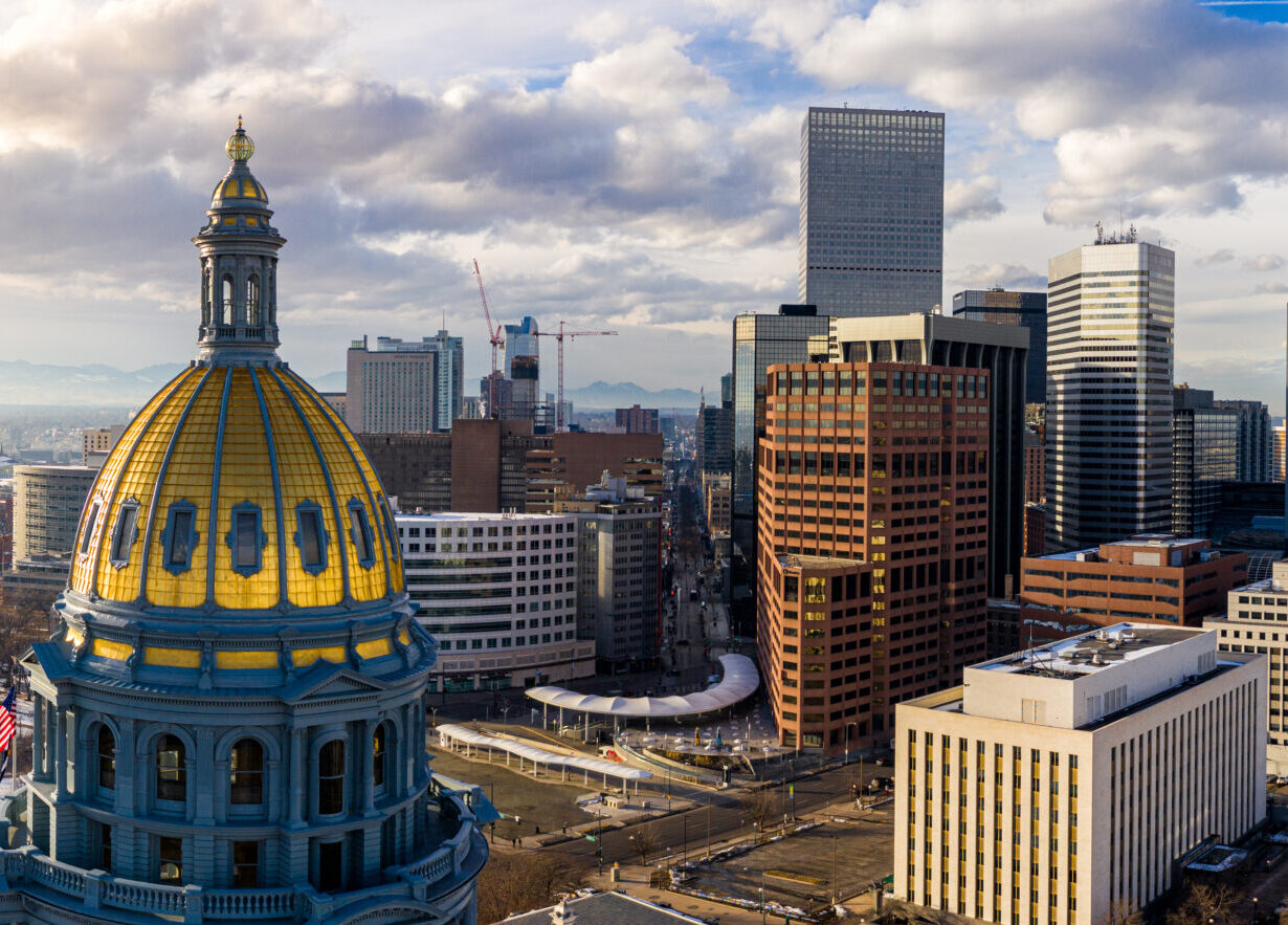The gold dome of the Colorado State Capitol in the foreground with the Denver skyline behind it