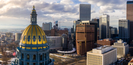 The gold dome of the Colorado State Capitol in the foreground with the Denver skyline behind it