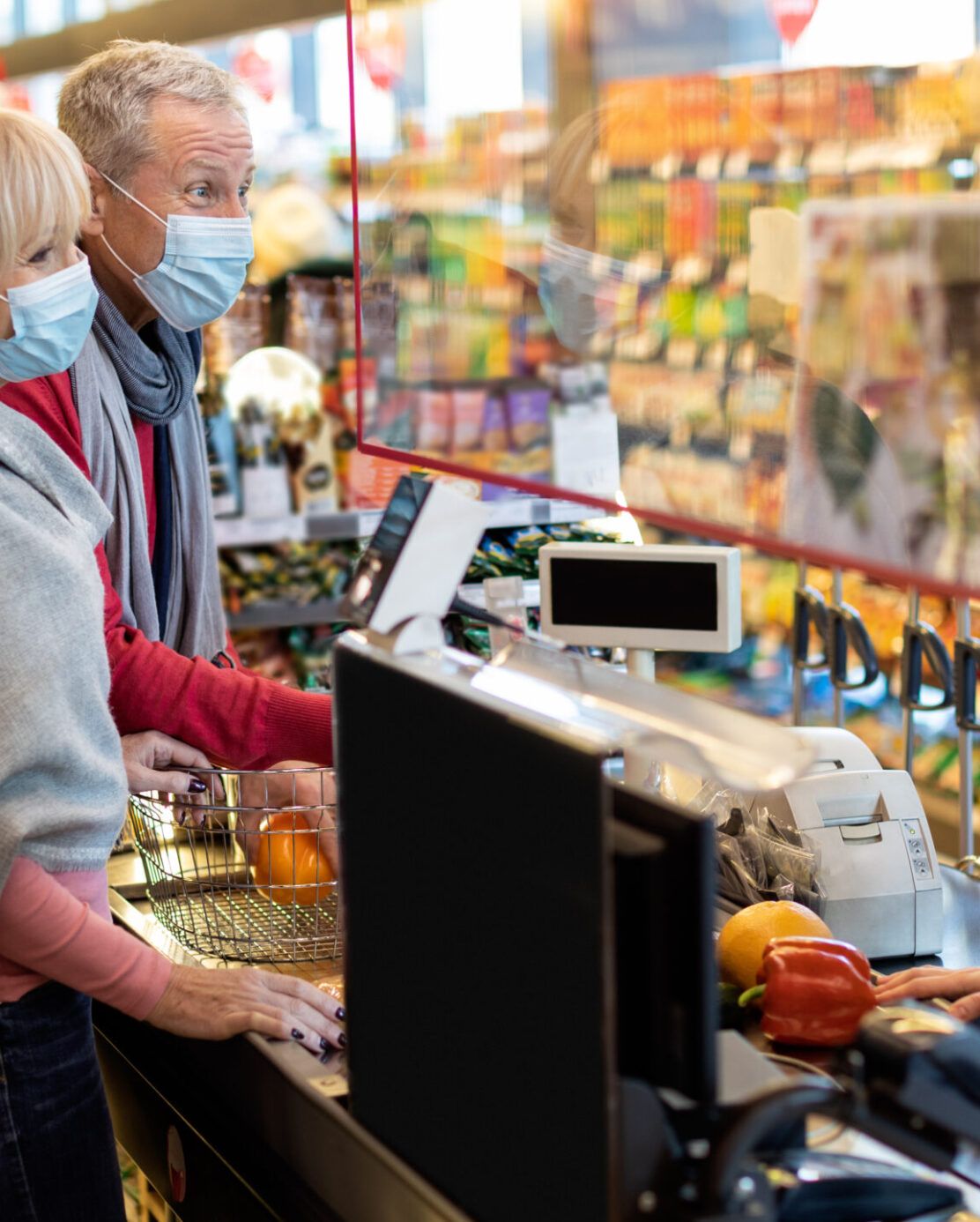 An older couple wearing face masks at the grocery store checkout stand