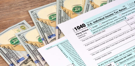 A 1040 individual tax return form on top of a pile of U.S. $100 bills.
