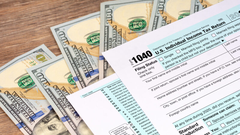 A 1040 individual tax return form on top of a pile of U.S. $100 bills.