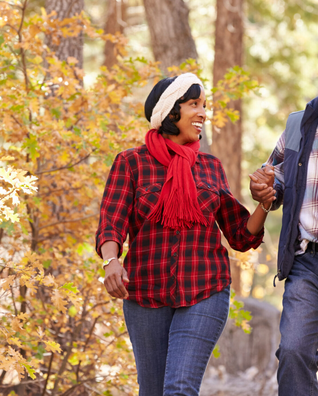 A Black couple holds hands while walking through fall foliage