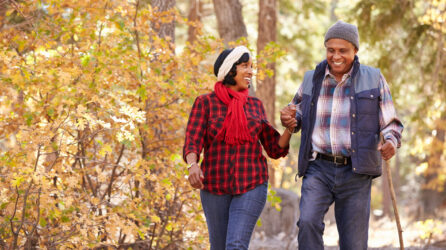 A Black couple holds hands while walking through fall foliage