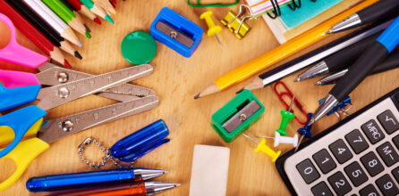 A variety of school supplies scattered on a table alongside a calculator.