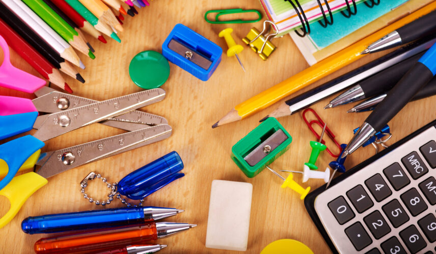 A variety of school supplies scattered on a table alongside a calculator.